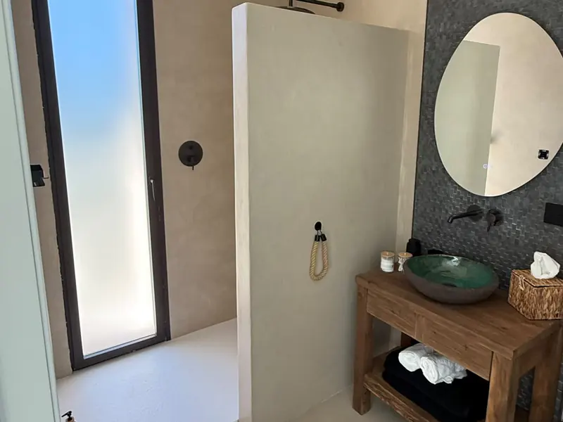 Baño con ducha de obra, murete y suelo continuo de microcemento sin juntas